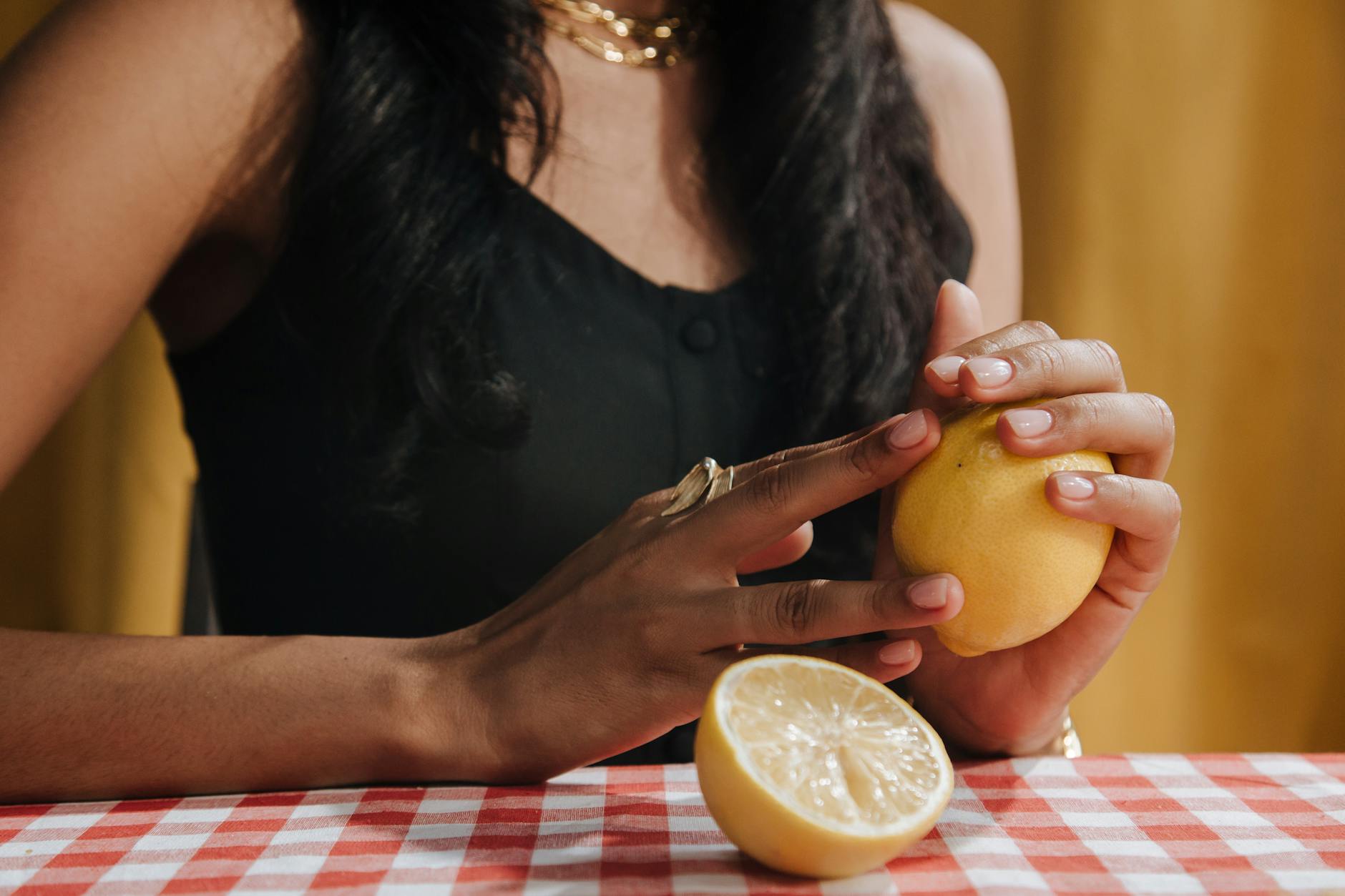 Una mano con uñas blancas sosteniendo un limón fresco en un fondo rosa suave, rodeada de tres limones adicionales