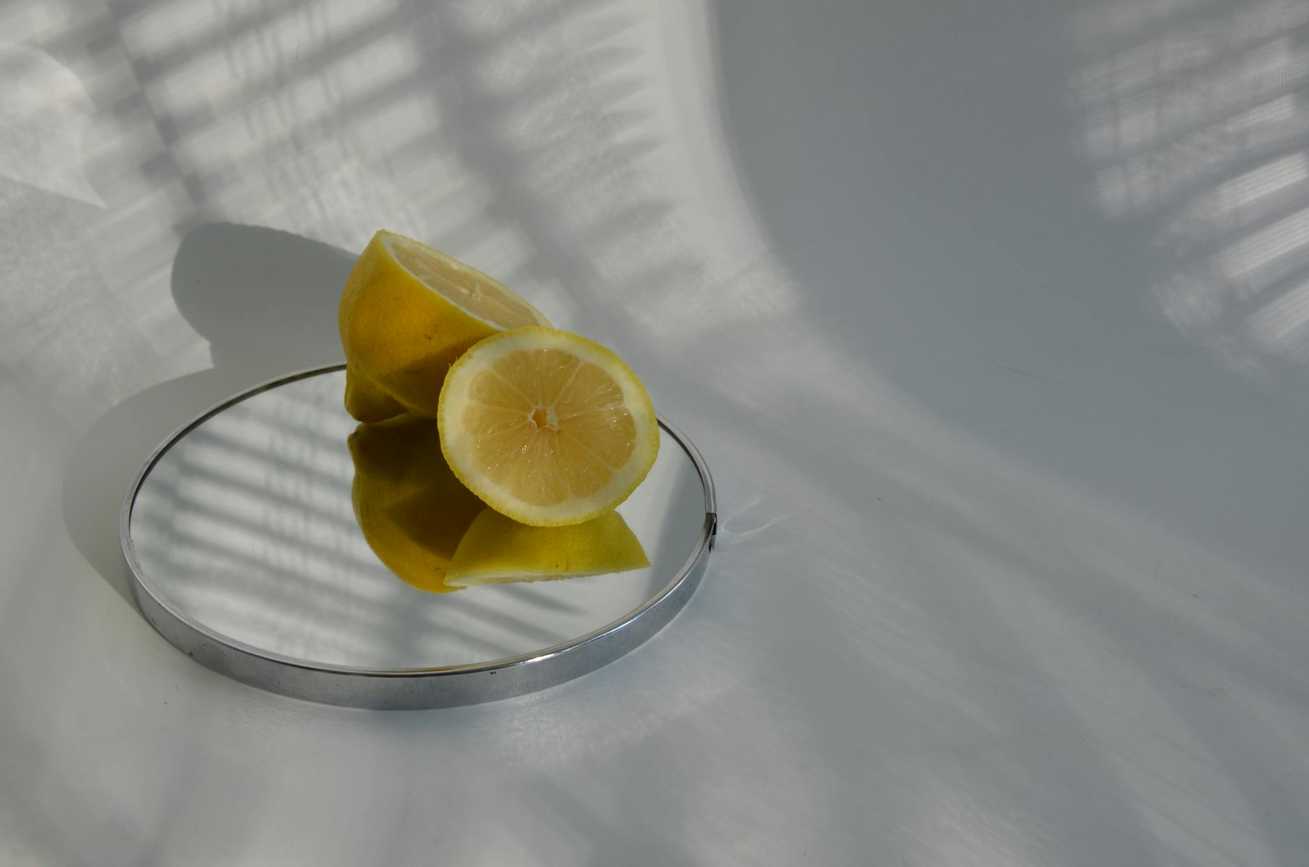 Composición minimalista con limones cortados sobre un espejo, con sombras dramáticas