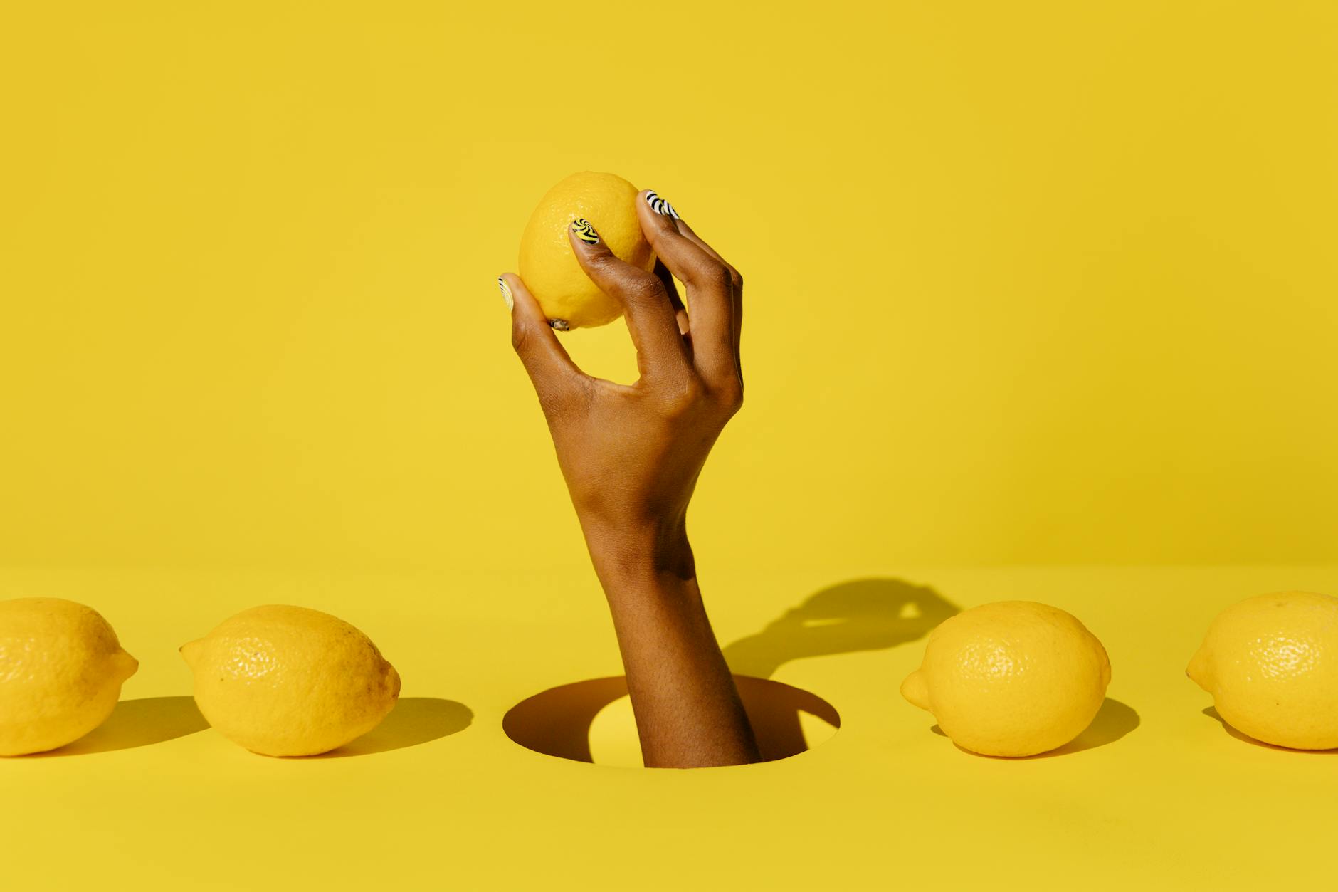 Mano sosteniendo un limón fresco sobre fondo amarillo vibrante, simbolizando frescura y sensibilidad sensorial