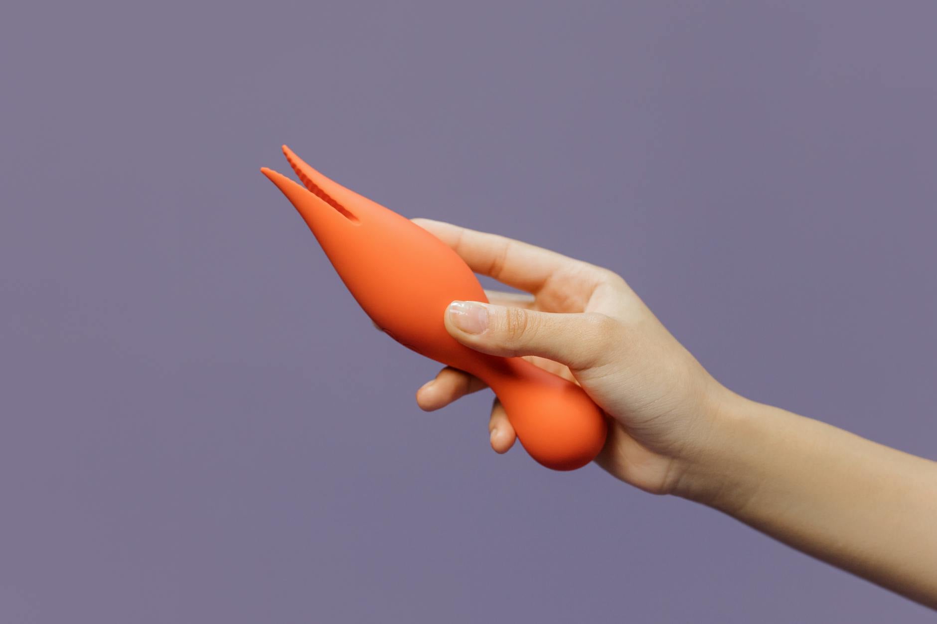 Mano sosteniendo un vibrador naranja moderno contra un fondo minimalista de color púrpura