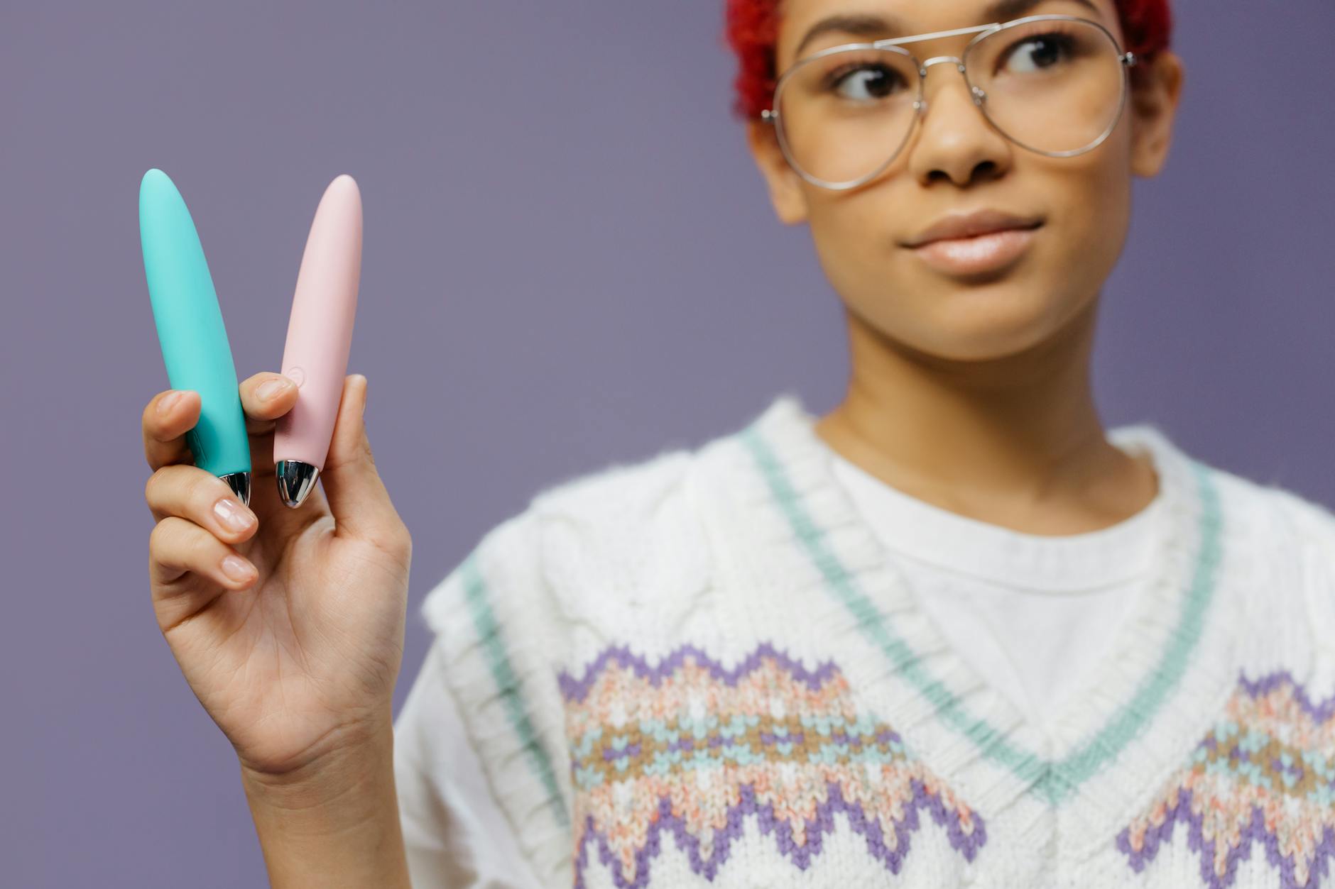 Mujer joven sosteniendo dos vibradores coloridos contra un fondo púrpura