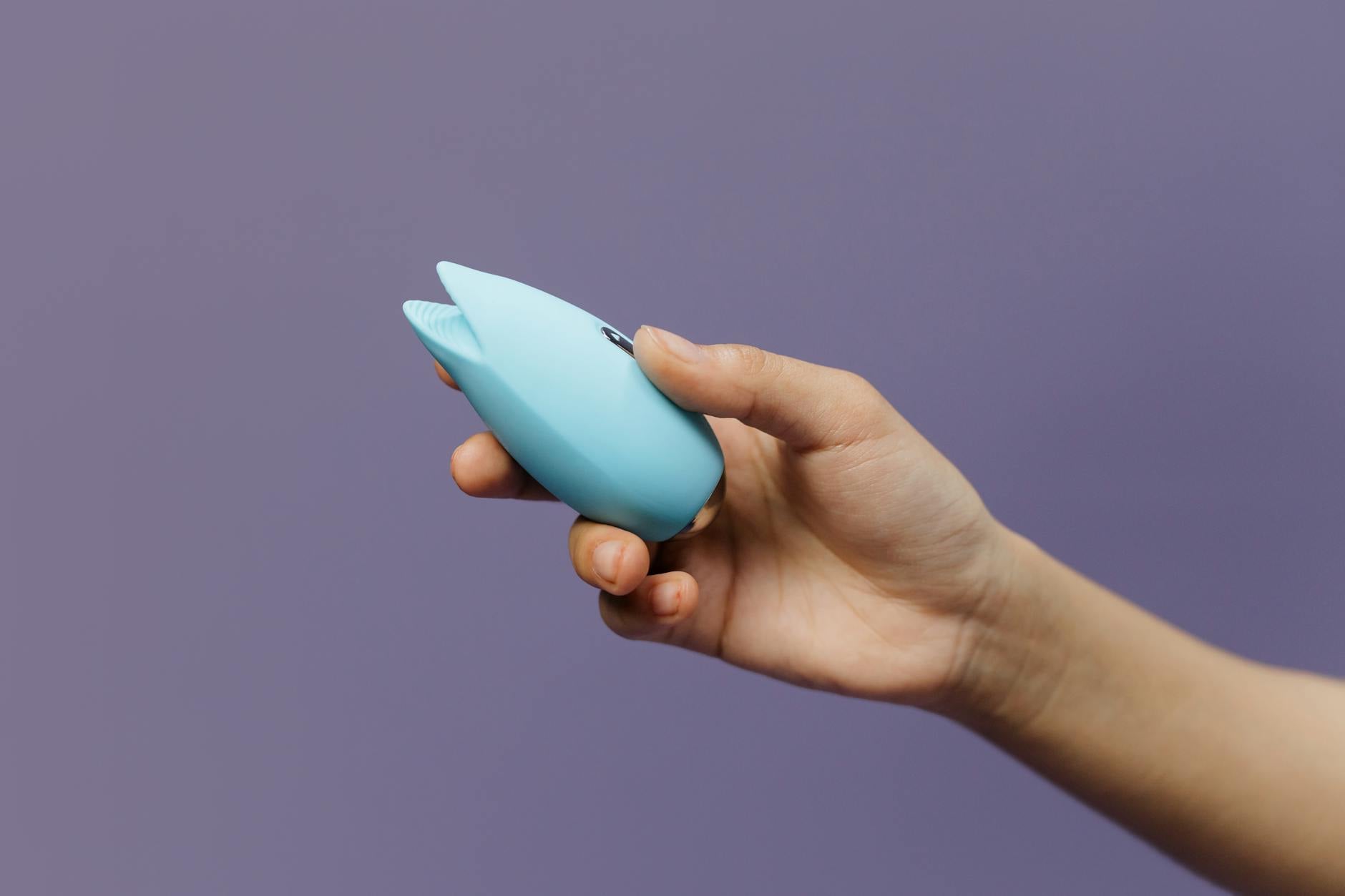 Vibrador de color azul sostenido en la mano contra fondo púrpura, promoviendo el amor propio y la sexualidad